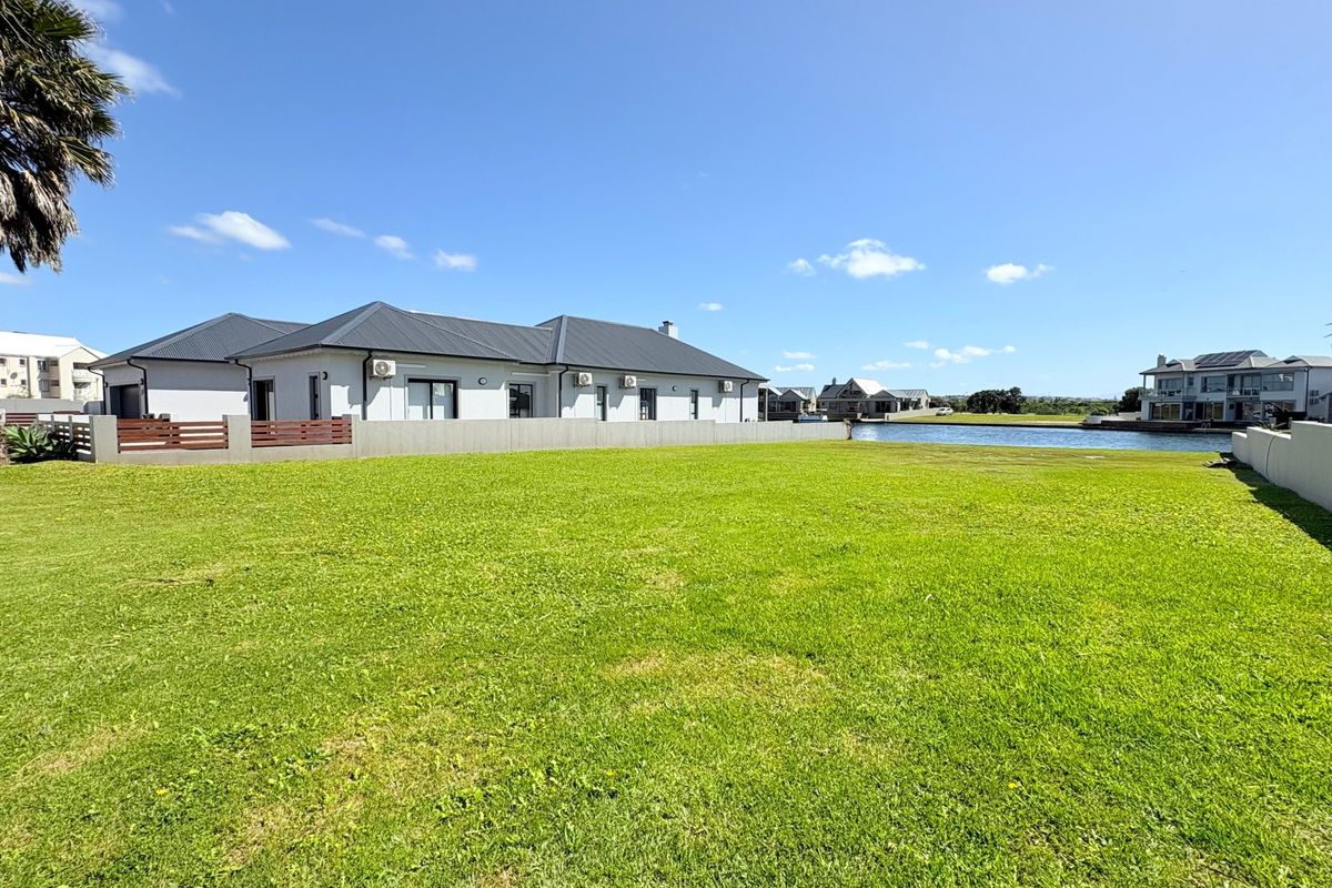 A spacious, well-maintained residential plot featuring a lush green lawn, boundary walls, and direct access to the waterfront.