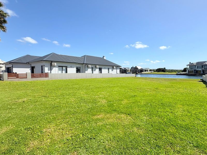 A spacious, well-maintained residential plot featuring a lush green lawn, boundary walls, and direct access to the waterfront.