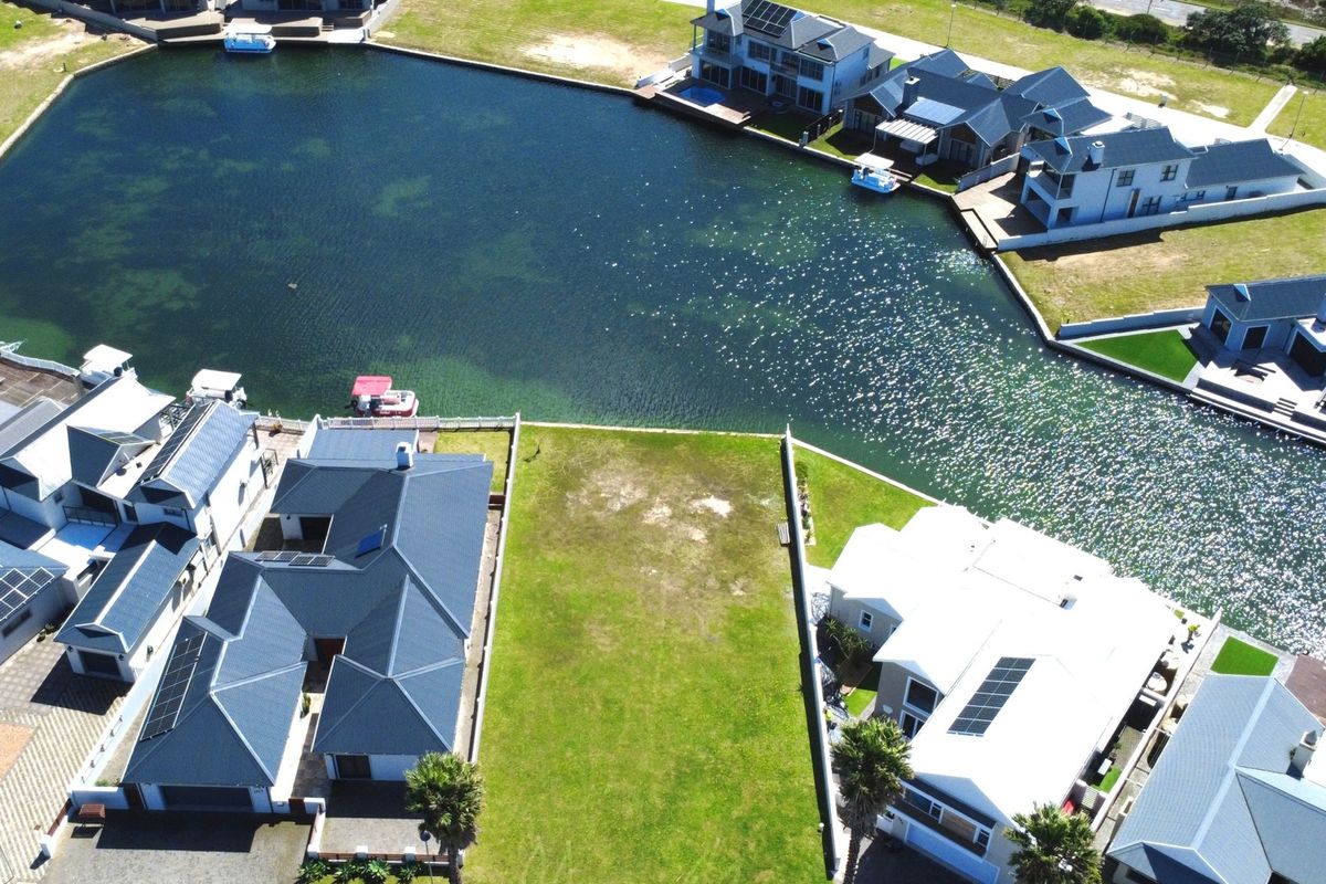 An aerial view of a vacant residential plot situated directly on a canal, surrounded by established luxury homes in a waterfront estate.