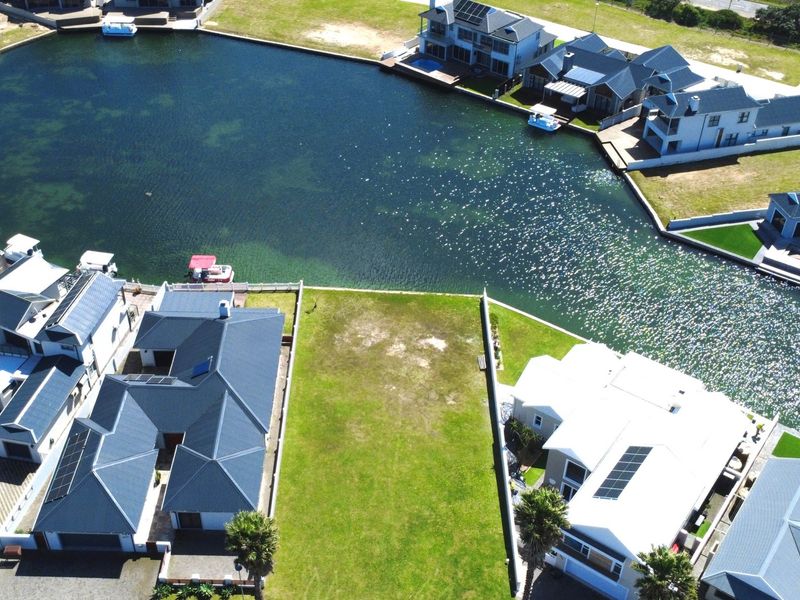 An aerial view of a vacant residential plot situated directly on a canal, surrounded by established luxury homes in a waterfront estate.