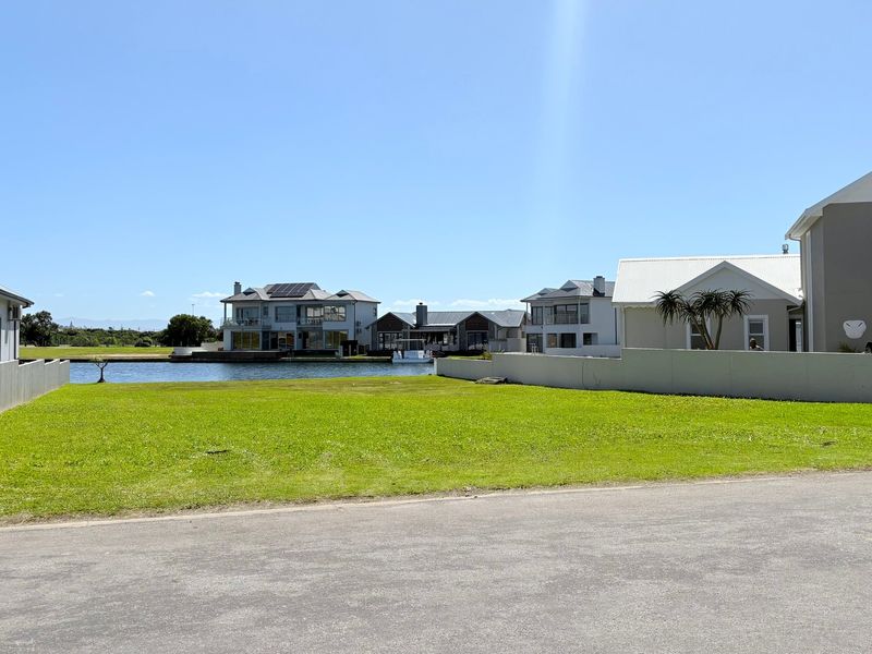 A vacant residential plot featuring a well-maintained lawn, boundary walls, and direct access to the waterfront in a developed estate setting.