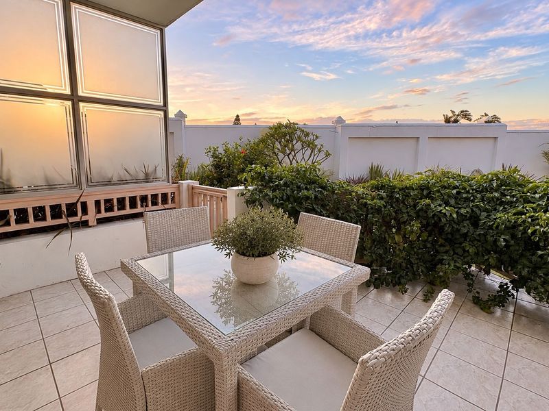 A well-maintained outdoor patio featuring tiled flooring, a frosted glass privacy screen, and a perimeter wall, perfect for sunset relaxation.