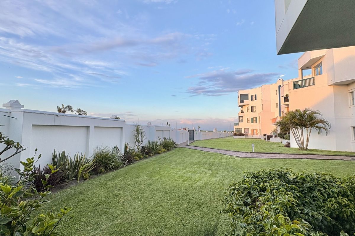 A well-maintained rear garden area featuring a manicured lawn, paved pathway, and boundary wall, adjacent to the apartment building exterior.