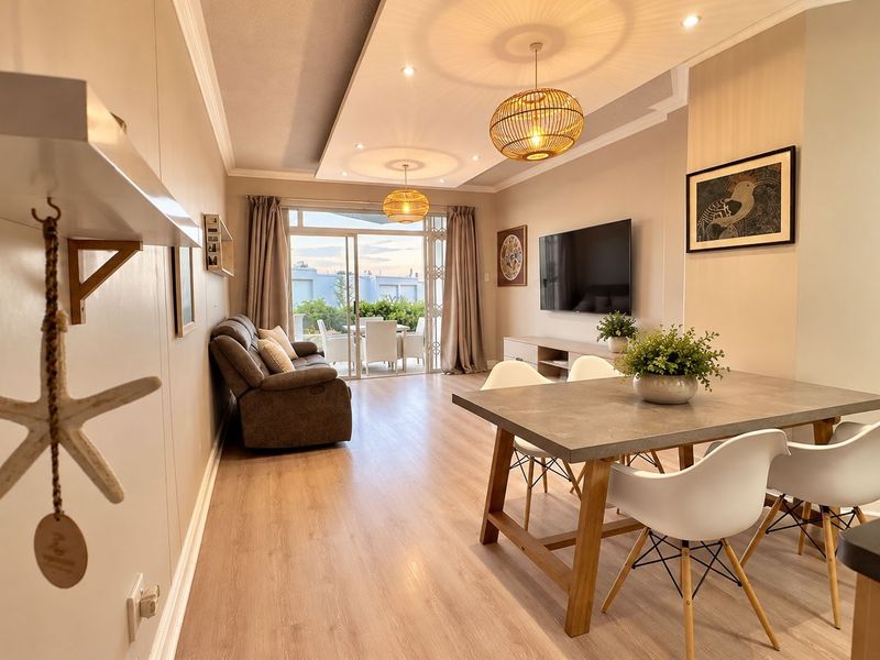 Spacious open-plan living and dining area featuring modern laminate flooring, recessed ceiling details, and large sliding glass doors leading to an outdoor patio.