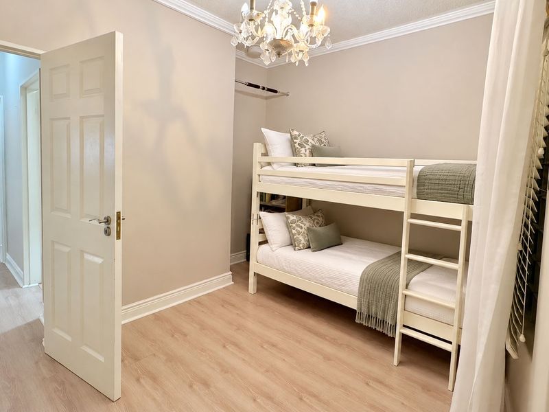A well-maintained bedroom featuring light-toned laminate flooring, crown molding, and a built-in closet rail, offering a clean and neutral living space.