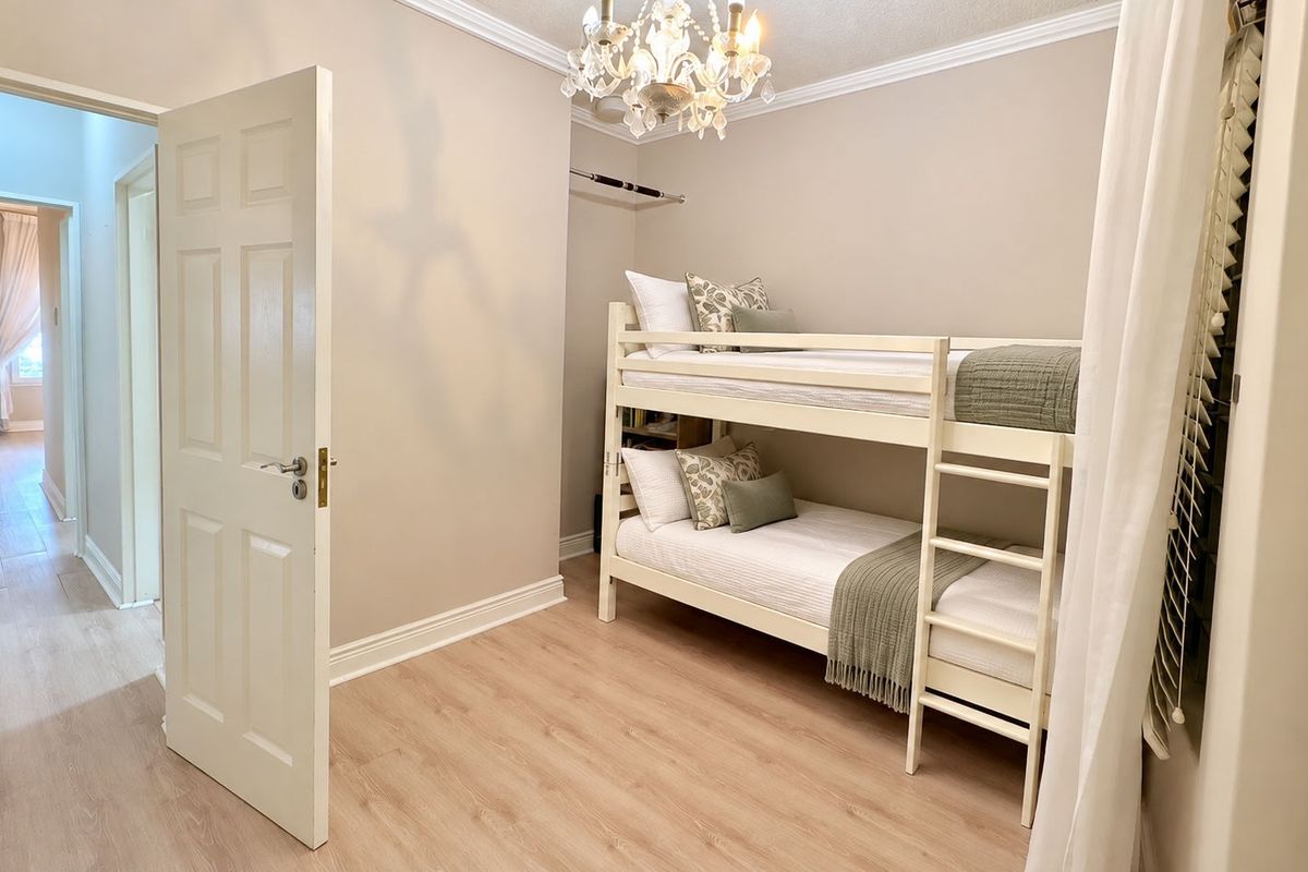 A well-maintained bedroom featuring light-toned laminate flooring, crown molding, and a built-in closet rail, offering a clean and neutral living space.