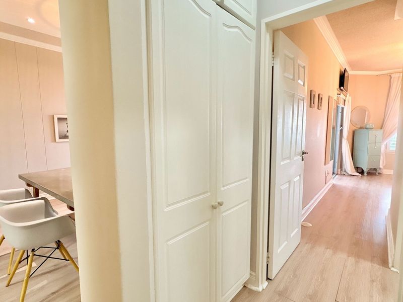 A bright hallway featuring light-toned laminate flooring, built-in storage cupboards, and classic coving, providing access to adjacent living and bedroom areas.