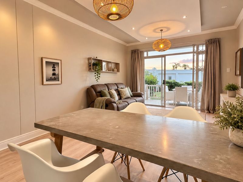 A bright open-plan living and dining area featuring modern laminate flooring, recessed ceiling lighting, and large sliding glass doors leading to an outdoor patio.