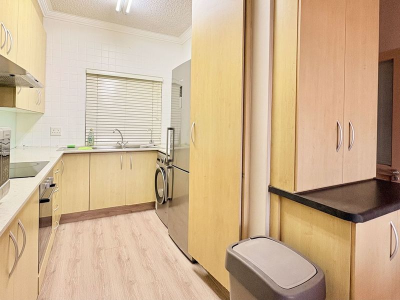A functional kitchen featuring light wood-finish cabinetry, laminate countertops, a tiled backsplash, and integrated appliances, offering a clean and practical workspace.