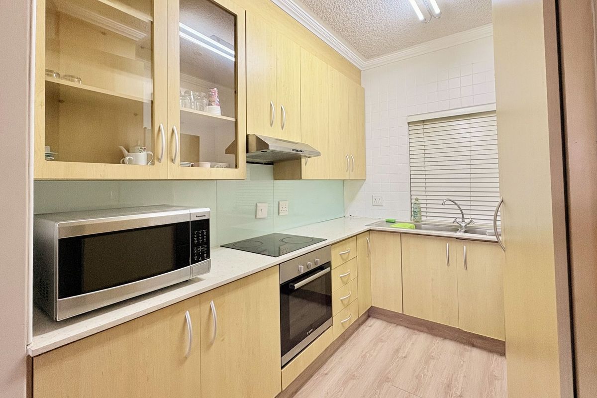 A functional kitchen featuring light wood-tone cabinetry, integrated appliances including an oven and hob, a tiled backsplash, and a stainless steel sink.