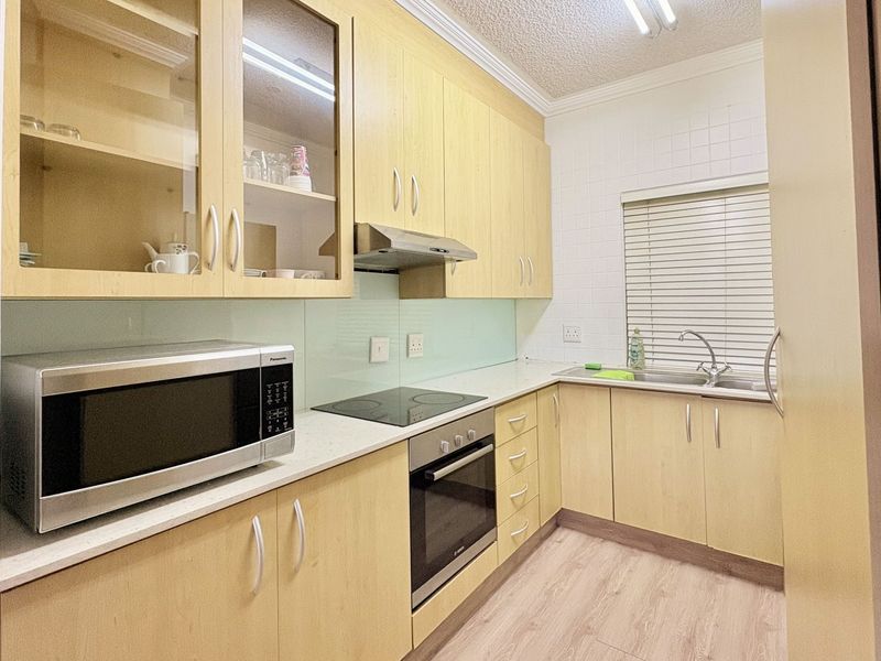 A functional kitchen featuring light wood-tone cabinetry, integrated appliances including an oven and hob, a tiled backsplash, and a stainless steel sink.