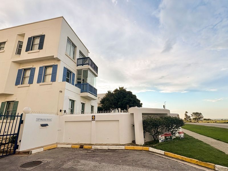 Exterior view of a multi-story apartment building featuring white facade, blue shutters, and secure boundary wall with gated entrance.