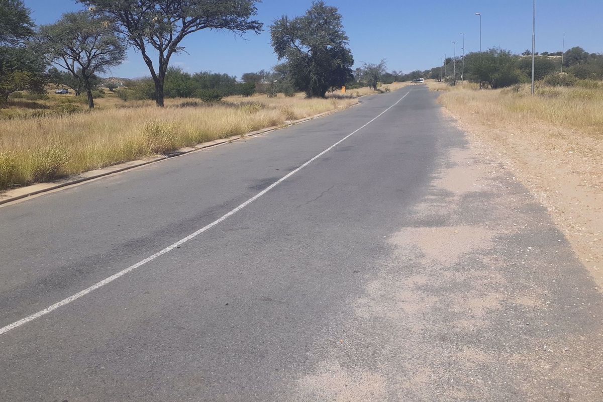 A view of the paved access road leading to the commercial vacant land, featuring street lighting and established roadside curbing.