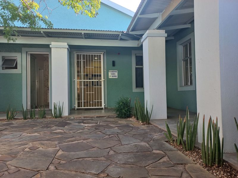 Front entrance of the office building featuring a covered porch, security gate, and stone paved courtyard area.