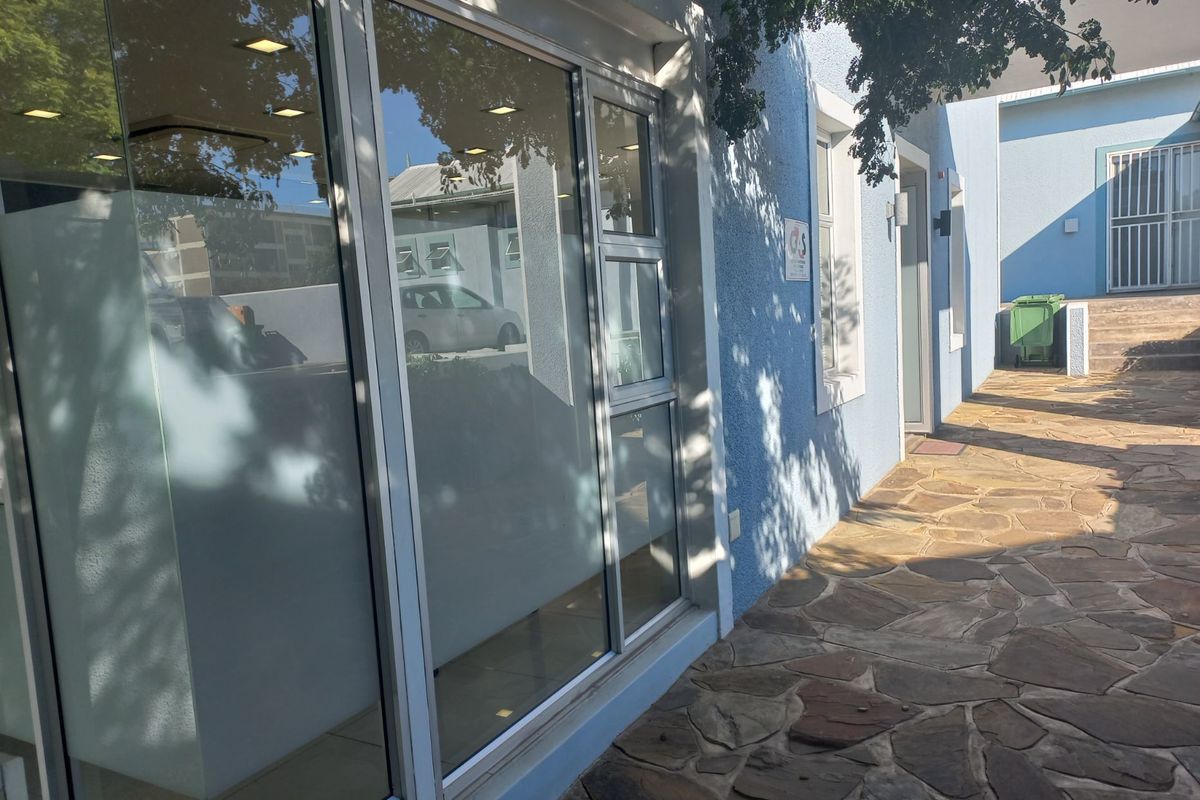 Exterior view of the office building entrance featuring stone paving, large glass storefront windows, and modern aluminium frames.