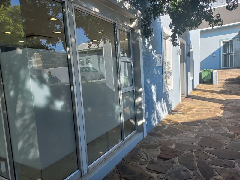 Exterior view of the office building entrance featuring stone paving, large glass storefront windows, and modern aluminium frames.