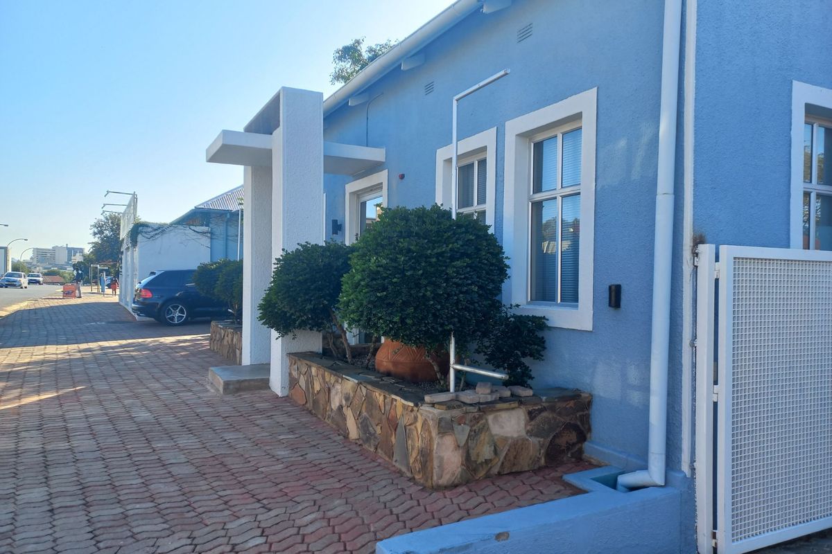 Front exterior view of a blue office building featuring a stone-clad planter box, paved driveway, and secure gated access.