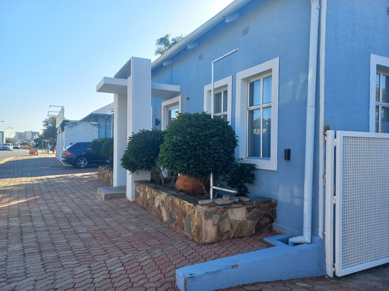 Front exterior view of a blue office building featuring a stone-clad planter box, paved driveway, and secure gated access.