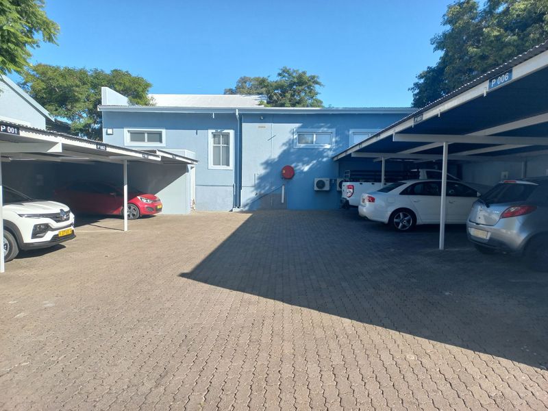 A paved outdoor parking area featuring multiple covered parking bays and external building infrastructure including air conditioning units.