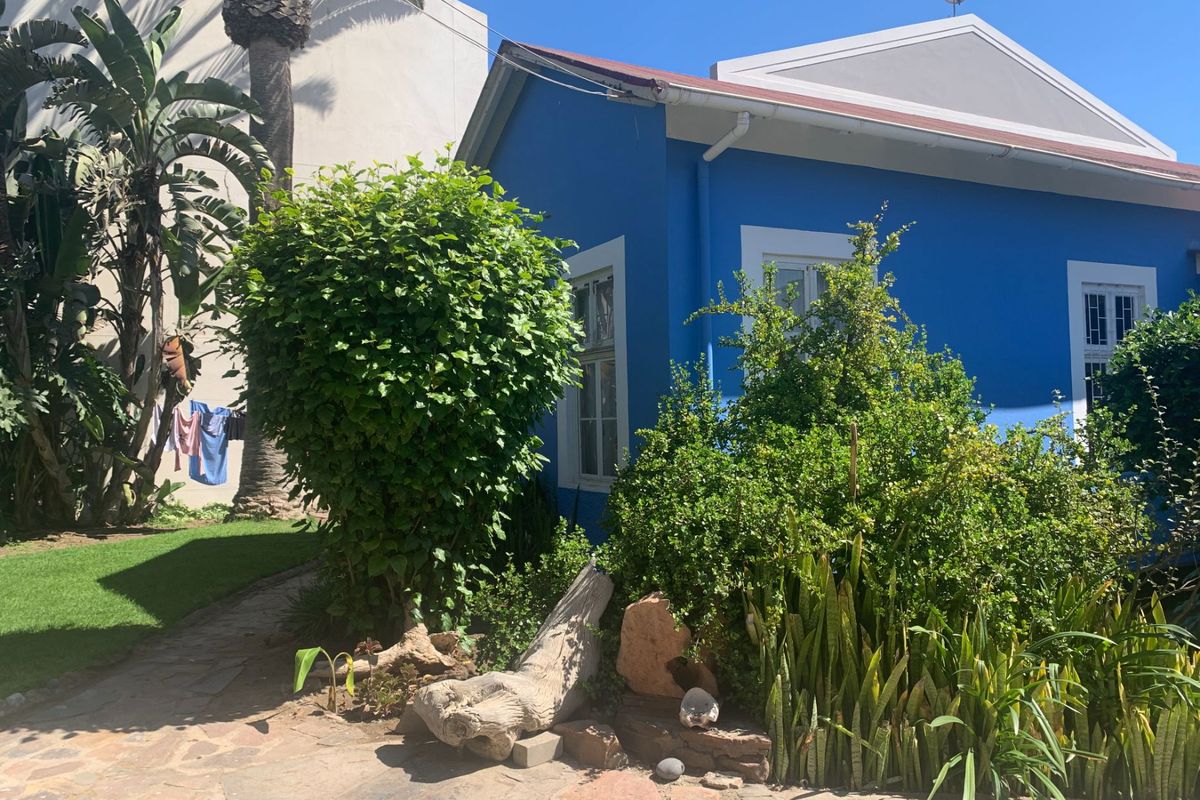 A view of the rear exterior of a blue-painted building featuring a stone-paved patio area and established garden landscaping.
