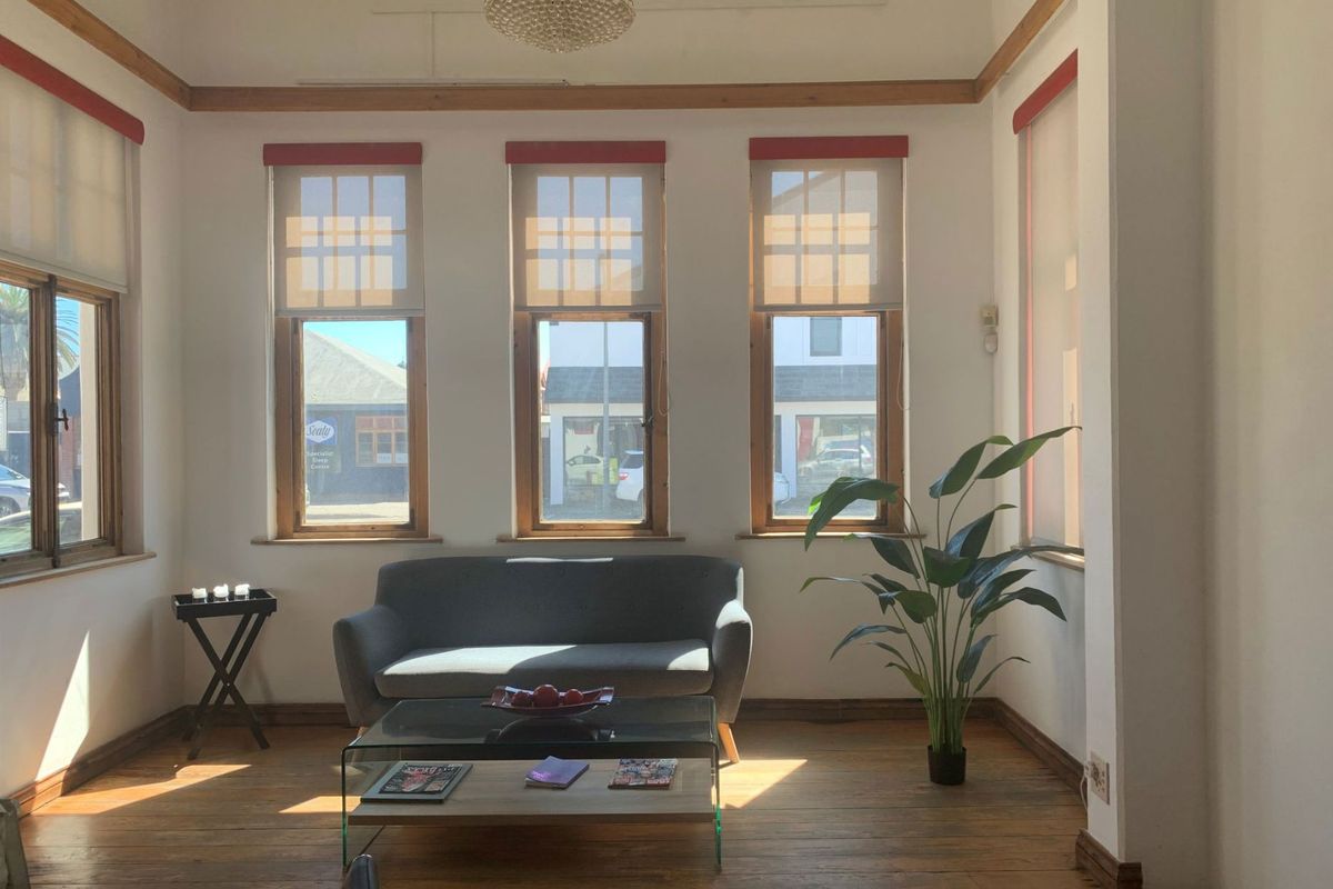 A bright living area featuring timber flooring, large sash windows with roller blinds, and decorative crown molding.