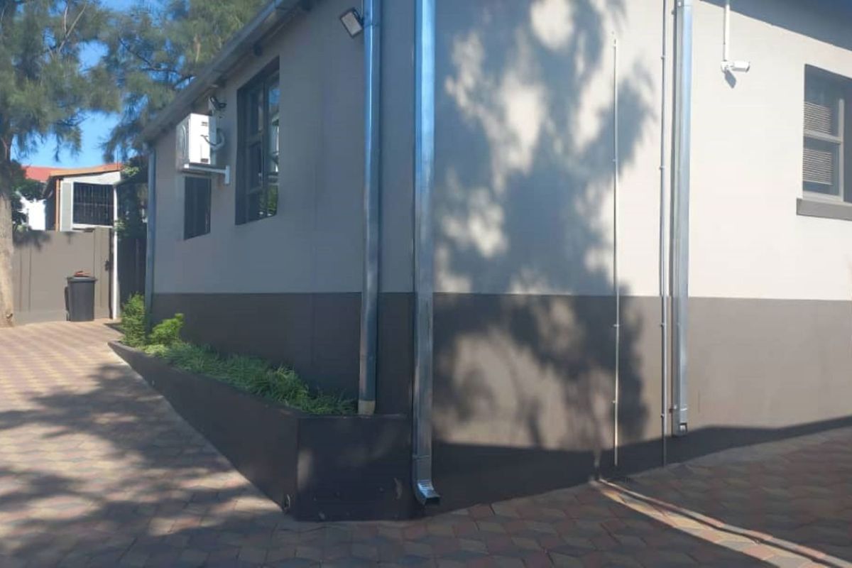 Exterior view of the office building featuring paved driveway, external air conditioning units, security lighting, and integrated planter boxes.