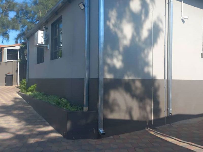 Exterior view of the office building featuring paved driveway, external air conditioning units, security lighting, and integrated planter boxes.