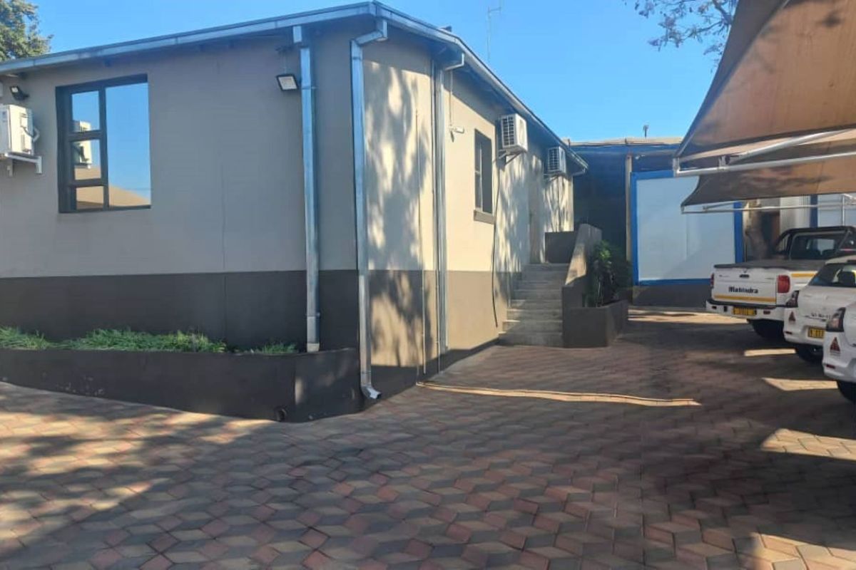 Rear exterior view of the office building featuring a paved driveway, covered parking area, and external access staircase.