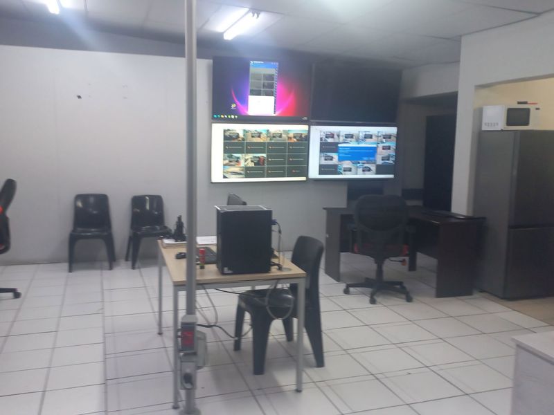 Functional office space featuring tiled flooring, suspended ceiling, and wall-mounted monitoring screens, suitable for administrative or security operations.