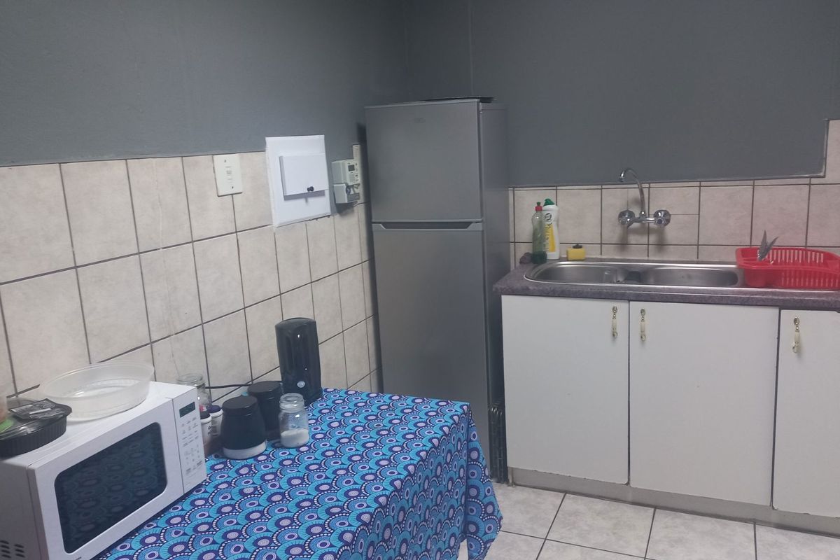 A compact office kitchenette featuring a double sink, tiled backsplash, and built-in cabinetry with visible wear on the cabinet doors and countertop.