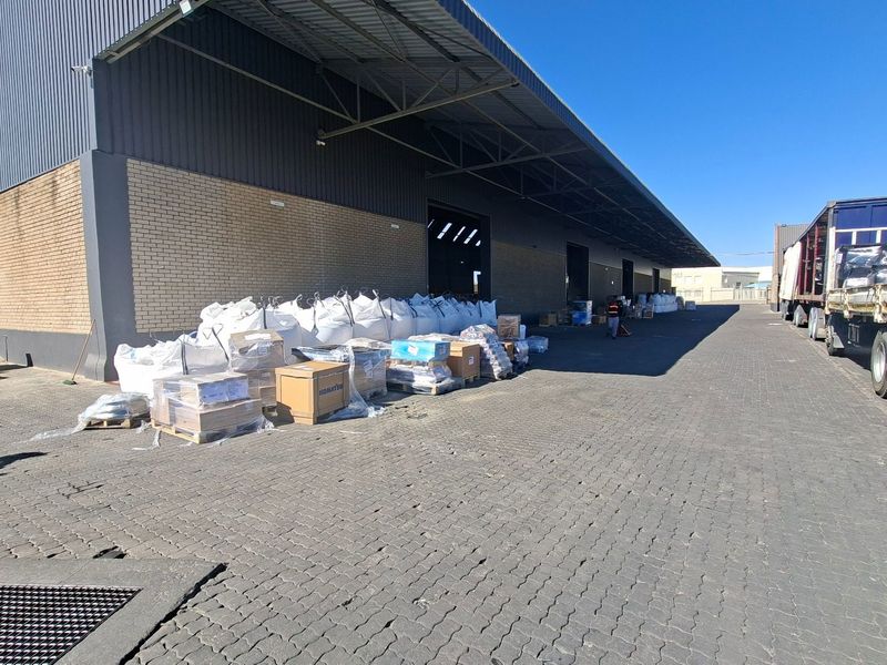 Industrial warehouse exterior featuring a large covered loading bay, brick and metal cladding, and an expansive paved yard area for logistics operations.