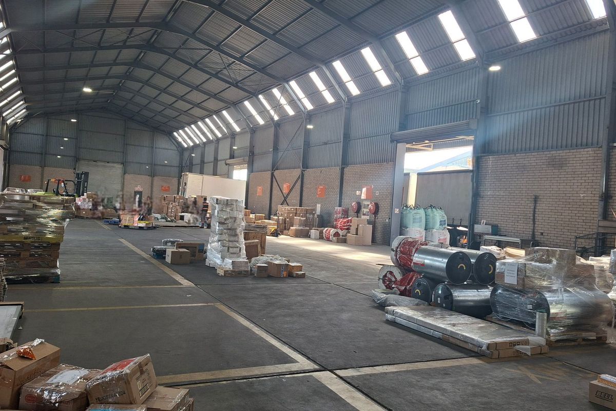 Spacious industrial warehouse featuring high-clearance corrugated metal roofing, skylights, exposed brick walls, and durable concrete flooring suitable for storage or manufacturing operations.