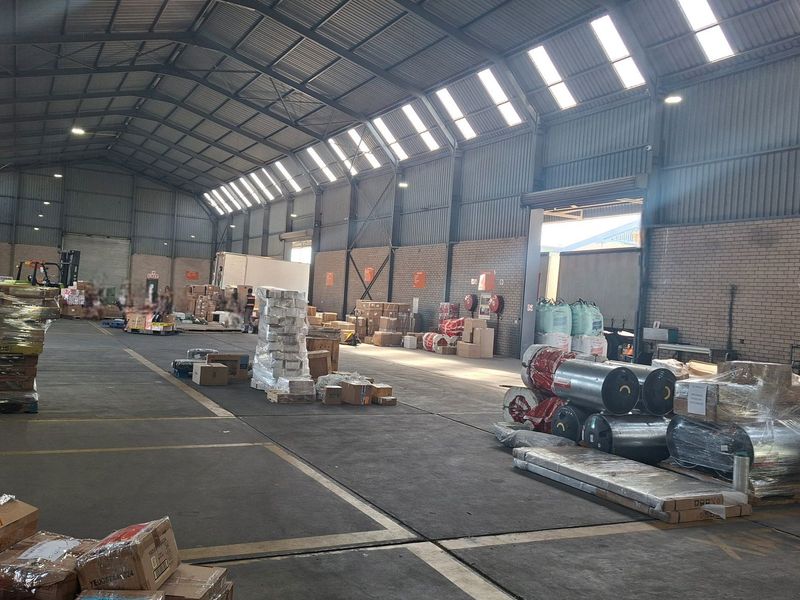 Spacious industrial warehouse featuring high-clearance corrugated metal roofing, skylights, exposed brick walls, and durable concrete flooring suitable for storage or manufacturing operations.
