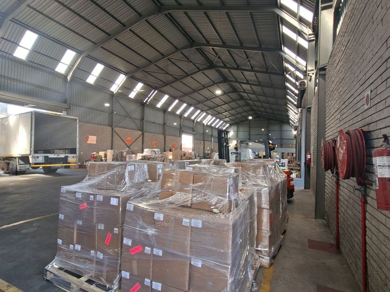 Spacious industrial warehouse featuring high-clearance steel truss roofing, integrated skylights, durable concrete flooring, and wall-mounted fire safety equipment.