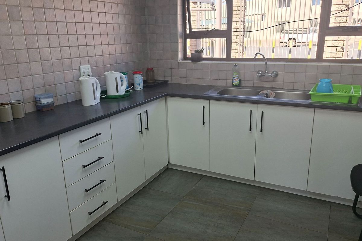 A functional kitchen area featuring white cabinetry, dark laminate countertops, a double stainless steel sink, and neutral tiled splashbacks.