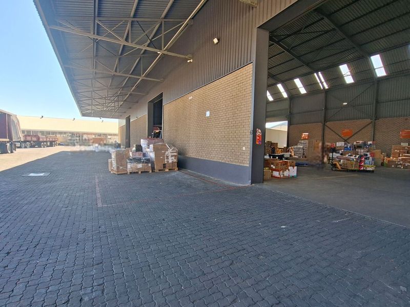 Industrial warehouse facility featuring a large paved loading yard, covered loading bay, and high-clearance steel structure with brick exterior walls.