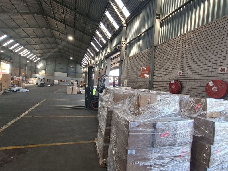Spacious industrial warehouse featuring high-clearance ceilings with skylights, exposed brick walls, concrete flooring, and integrated fire safety equipment.