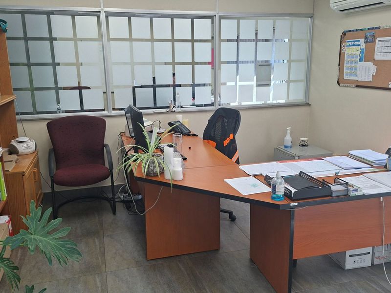 A functional office space featuring aluminum-framed glass partitioning, tiled flooring, and an integrated air conditioning unit.