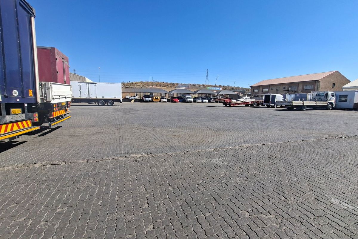 A large, paved industrial yard featuring multiple shade cloth carports and surrounding industrial warehouse structures.
