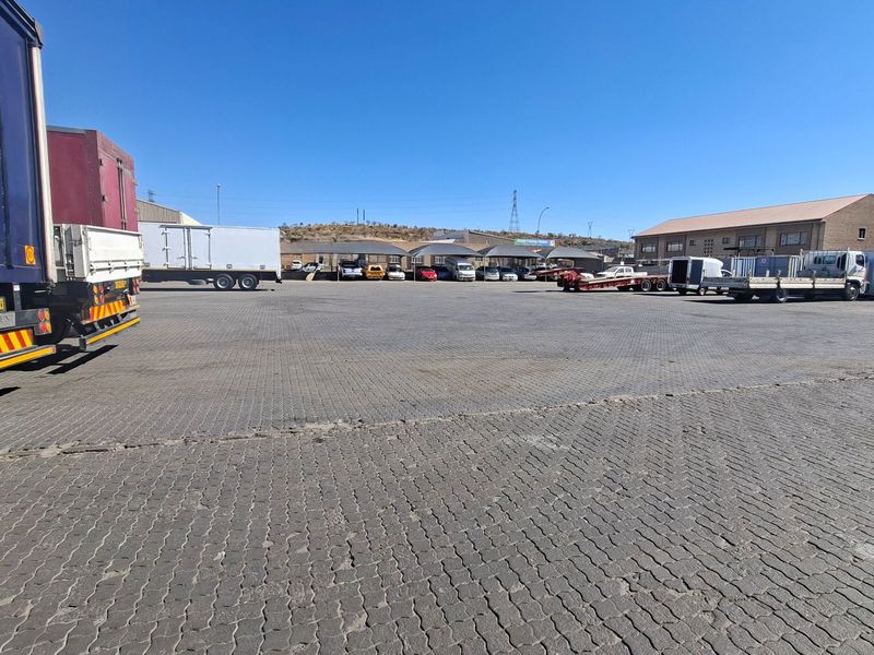 A large, paved industrial yard featuring multiple shade cloth carports and surrounding industrial warehouse structures.