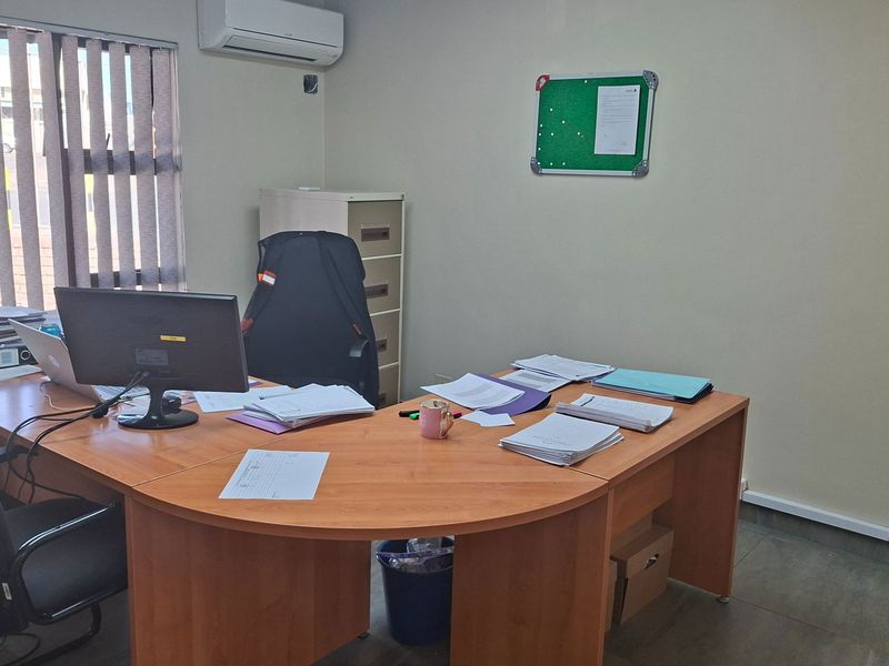 A functional office space featuring tiled flooring, vertical window blinds, and a wall-mounted split-system air conditioning unit.