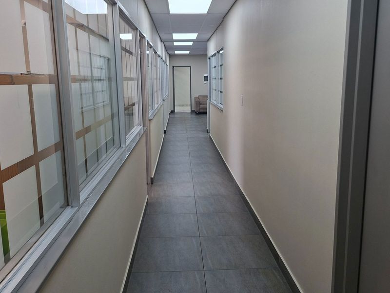 A clean, well-lit industrial hallway featuring modern grey floor tiles, recessed ceiling lights, and glass partition walls providing a professional aesthetic.