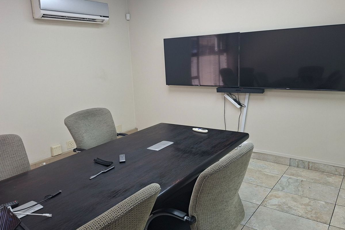 A functional office meeting room featuring tiled flooring, wall-mounted display screens, and a split-system air conditioning unit.