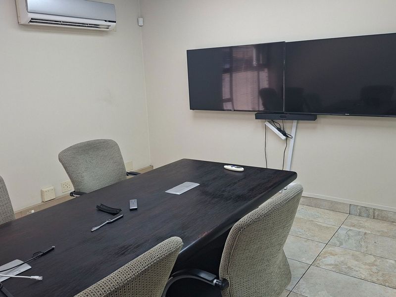 A functional office meeting room featuring tiled flooring, wall-mounted display screens, and a split-system air conditioning unit.