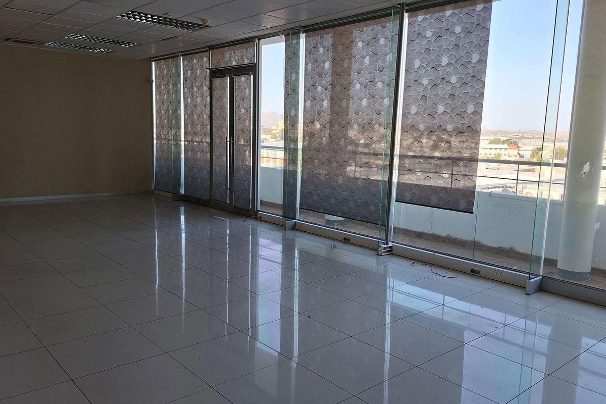 Spacious, empty office suite featuring large floor-to-ceiling glass windows, tiled flooring, and a suspended ceiling with integrated lighting.