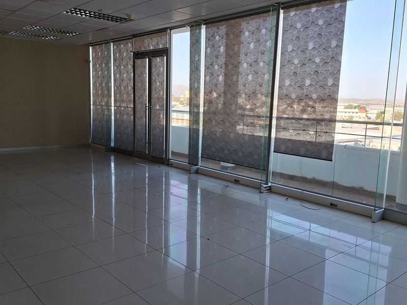 Spacious, empty office suite featuring large floor-to-ceiling glass windows, tiled flooring, and a suspended ceiling with integrated lighting.