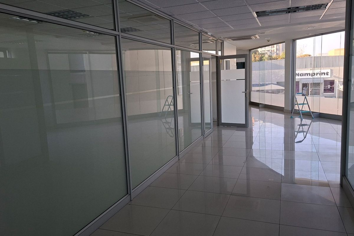 Modern vacant office space featuring glass partition walls, polished tiled flooring, and a suspended ceiling with recessed lighting.
