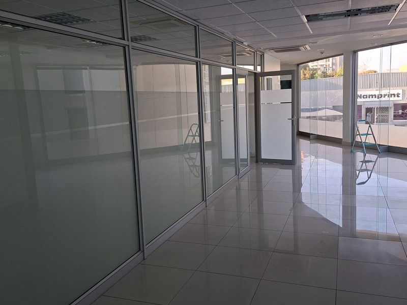 Modern vacant office space featuring glass partition walls, polished tiled flooring, and a suspended ceiling with recessed lighting.