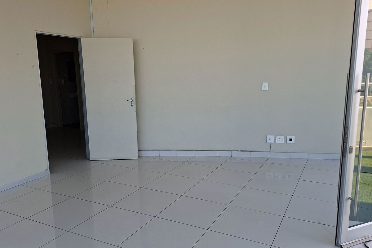 A bright, empty office space featuring neutral tiled flooring, clean walls, and a glass sliding door providing access to an outdoor area.