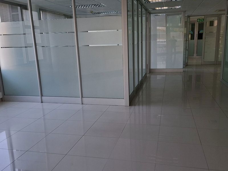 A bright, modern office space featuring glass partitioning, polished tiled flooring, and a suspended ceiling with integrated lighting.